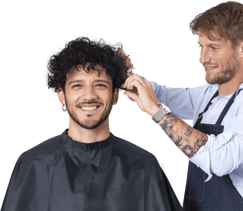 A barber trimming the hair of a smiling client in a black cape